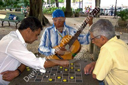 Man playing a guitar watches a checker game at a park in Rio de Janeiro, Brazil.