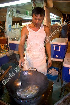 Chinese man cooking with a wok at a roulotte, food van in Papeete on the island of Tahiti.