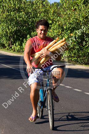Tahitian man carrying baguettes while riding a bicycle on the island of Moorea.
