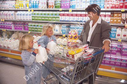 Twin girls shopping for milk with their mother in a grocery store.