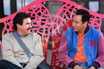 Mexican men talk while sitting on a public art bench along the Paseo de la Reforma in Mexico City, Mexico.