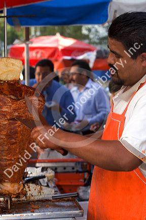 Street vendor cooking and cutting meat for souvlaki in Mexico City, Mexico.