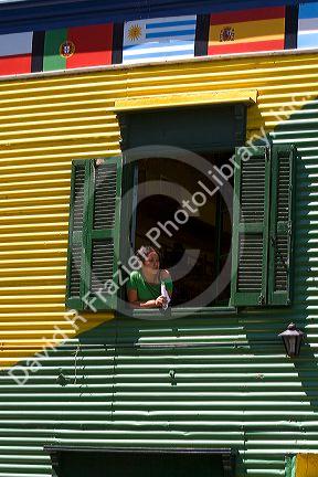 Woman looking out the window of a colorful building in the La Boca barrio of Buenos Aires, Argentina.