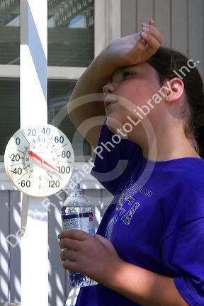 11 year old girl drinking water below a thermometer reading 100 degrees fahrenheit on a hot summer day in Boise, Idaho. MR