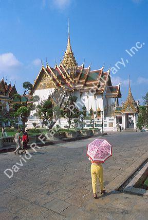 Woman walking with an umbrella in front of the Grand Palace in Thailand.