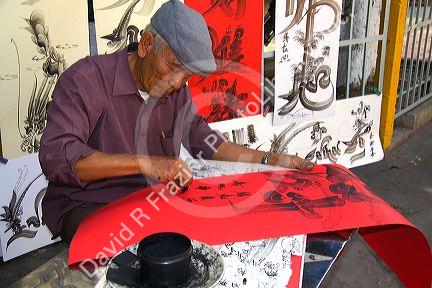 Vietnamese man drawing Chinese characters on red paper for good luck at the Giac Lam Pagoda Buddhist temple in Ho Chi Minh City, Vietnam.