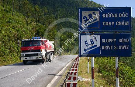 Fuel truck traveling past a grade warning road sign along the Hai Van Pass in Thua Thien-Hue Province, Vietnam.