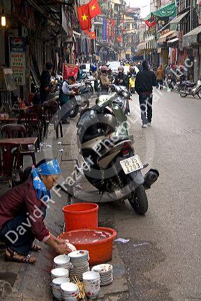 Vietnamese woman washing dishes on the street in Hanoi, Vietnam.