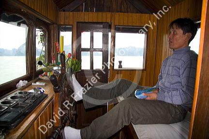 Vietnamese boat captin steering with his feet in Ha Long Bay, Vietnam.