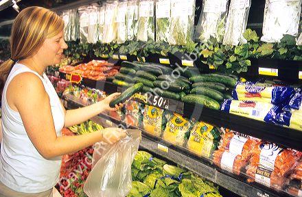 Woman shopping for cucumbers in the produce section of a grocery store.