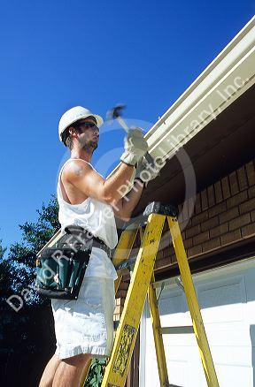 Worker putting on gutters and downspouts on a house.