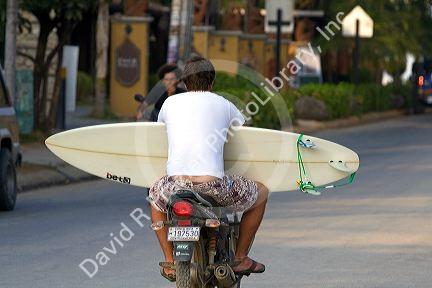 Man riding a scooter carries a surf board in the town of Tamarindo on the Northern Pacific Coast of Costa Rica.