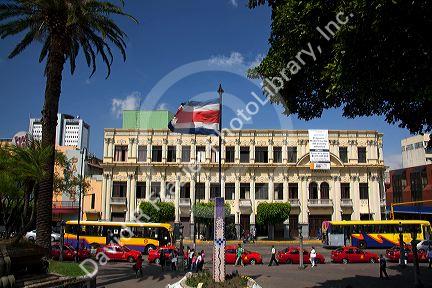Costa Rican flag, red taxicabs, and yellow buses at the Parque Central in the city of San Jose, Costa Rica.