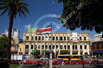 Costa Rican flag, red taxicabs, and yellow buses at the Parque Central in the city of San Jose, Costa Rica.
