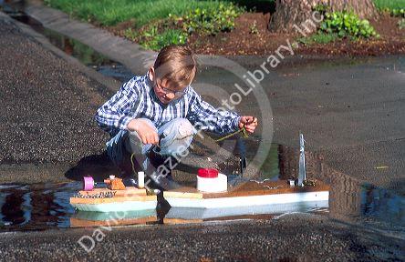 Six year old boy floating a home made model boat.  MR