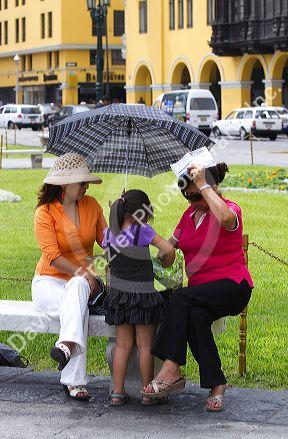 Women shading themselves from the hot sun with an umbrella at the Plaza Mayor or Plaza de Armas of Lima, Peru.