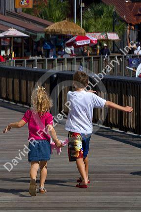 Brother and sister run on the boardwalk at Johns Pass Village located on the waterfront at Madeira Beach, Florida, USA.