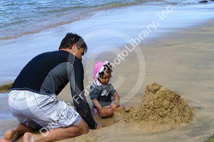 Father and daughter play in the sand on the island of Kauai, Hawaii, USA.