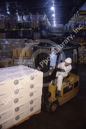 A worker using a forklift to move a pallet of cheese being stored in a refrigerated warehouse.