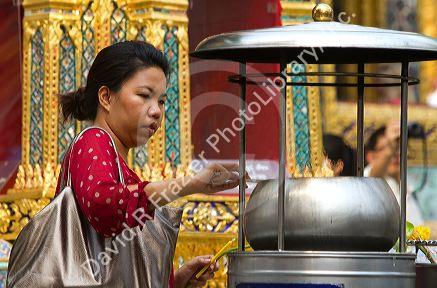 Woman lighting incense at the Temple of the Emerald Buddha located within the precincts of the Grand Palace, Bangkok, Thailand.