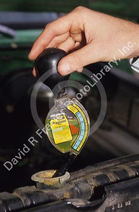 Person using a hydrometer to check the anti-freeze level on an automobile radiator.