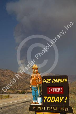 Smokey Bear extreme fire danger sign with a plume of smoke from a forest fire in the background in Boise County, Idaho, USA.