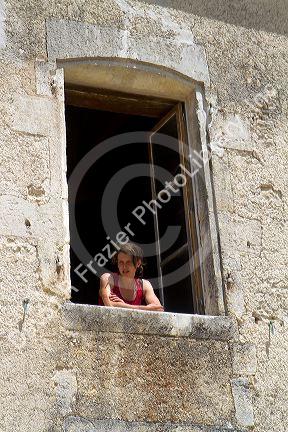 Young woman looks out the window of a french farm house near Angouleme in southwestern France.