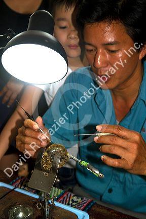 Worker on a pearl farm placing sand in an oyster shell to grow a cultured pearl, Ha Long Bay, Vietnam.