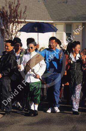 Laotian wedding procession in Boise, Idaho. The groom is escorted to the bride's house for the wedding ceremony by friends and relatives. Groom is dressed in traditional attire walking through a modern american suburban housing development.