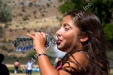 Young hispanic girl drinking water out of a bottle.