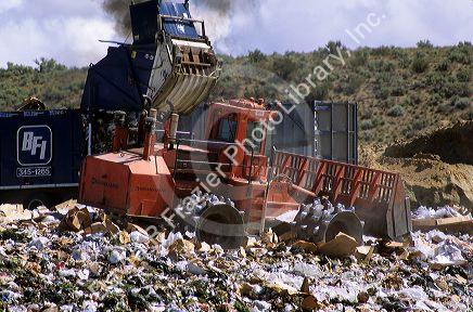 A large dumpster unloads trash while a bulldozer moves it at a sanitary landfill in Boise, Idaho.