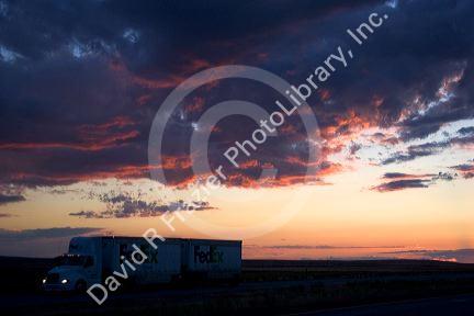 Automobiles and long haul trucks driving with headlights on at sunset in Idaho.