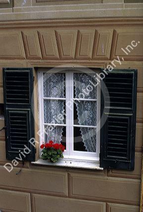 A window framed with green shutters and flowers on the Ligurian Coast of Italy.