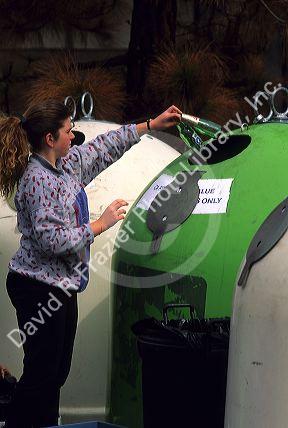 A woman depositing colored glass bottles into a recycling bin at a recycle center.