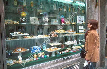 Woman looking through a bakery window at pastrie  and candy in Madrid, Spain.