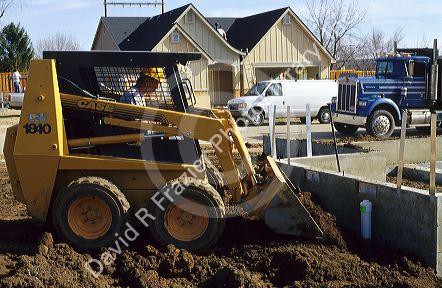 Construction worker using a bobcat type tractor to backfill a foundation in Boise, Idaho.