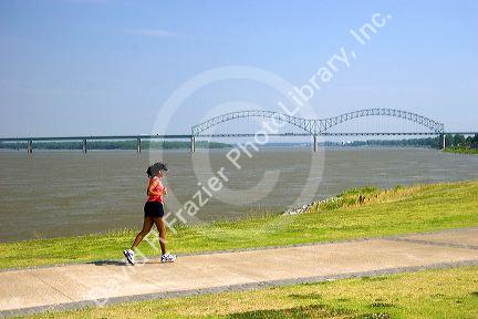 Woman jogging along the Mississippi River levee with the Hernando Desoto Memorial Bridge in the background at Memphis, Tennessee.