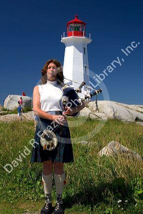Scottish woman in traditional dress playing the bag pipes in front of a lighthouse at Peggy's Cove, Nova Scotia, Canada.