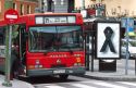 Bus driving on the streets of Madrid, Spain.  Bus stop showing signage of the black ribbon mourning the tragedy of the train bombings on March 11, 2004.