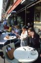 A women using a cell phone at a sidewalk cafe in Paris, France.