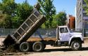 Dump truck with raised bed dumping dirt.