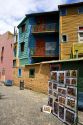 Paintings being sold on Caminito street in front of colorful buildings in the La Boca area of Buenos Aires, Argentina.