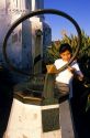 A young girl stands near a sundial pointing to the time indicated by the shadow line in Los Angeles, California.