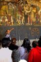 A tour guide showing tourists a mural painted by Diego Rivera at the National Palace in Mexico City, Mexico.