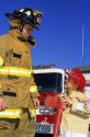 7 year old boy looks up to a firefighter while dressed in his home made Halloween costume as a firefighter in Boise, Idaho, USA.