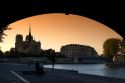 View of the Notre Dame cathedral at sunset through the arch of the Tournelle Bridge on the River Seine in Paris, France.