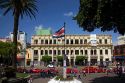Costa Rican flag, red taxicabs, and yellow buses at the Parque Central in the city of San Jose, Costa Rica.