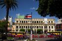 Costa Rican flag, red taxicabs, and yellow buses at the Parque Central in the city of San Jose, Costa Rica.