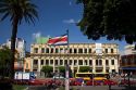 Costa Rican flag, red taxicabs, and yellow buses at the Parque Central in the city of San Jose, Costa Rica.