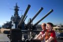 Grandfather and grandson look through the sight of a machine gun on the USS Alabama Battleship at Battleship Memorial Park, Mobile, Alabama, USA.